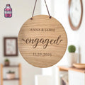 Round hanging wooden ornament engraved with names and an engagement date