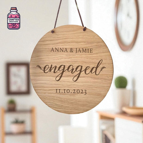 Round hanging wooden ornament engraved with names and an engagement date