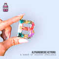Multicoloured resin letter keyring held between two fingers